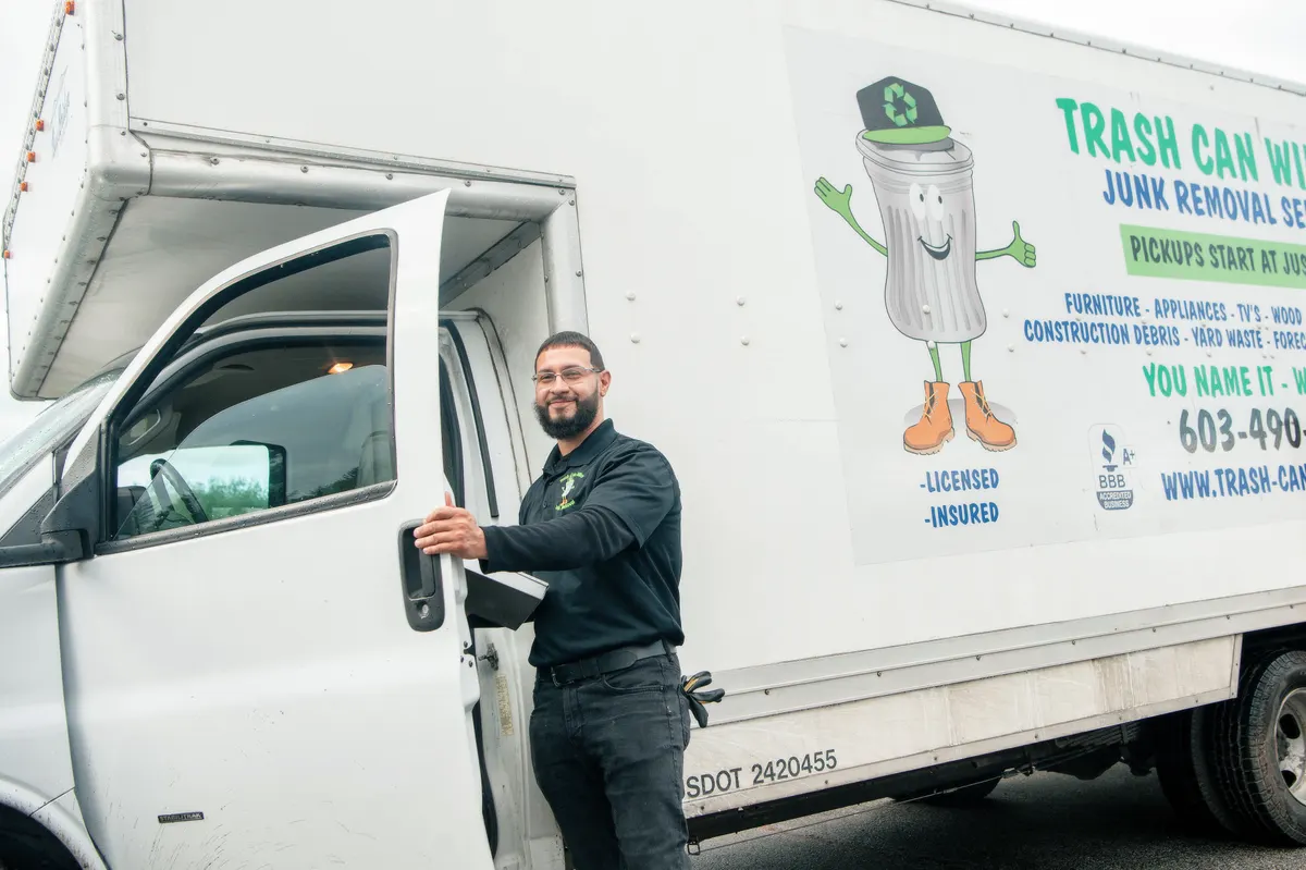 A crew member at the cab of a signwritten Trash Can Willy's box truck